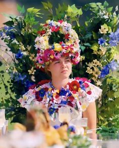 a woman sitting at a table with flowers in her hair and wearing a flower crown