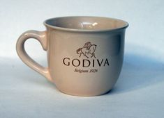 a white coffee cup with the word godiva on it and a horse in brown lettering