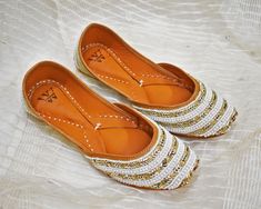 This Embellished Leather Indian Jutti flat is exclusively Handcrafted by specialized craftsmen in India inheriting this craft over generations. The jutti or Punjabi Jutti is a type of footwear common in North India and neighboring regions. They were traditionally made up of leather and with extensive embroidery, in real gold and silver thread as inspired by Indian royalty over 400 years ago. Step up your fashion game with these handmade leather juttis, designed to add a touch of tradition and st Traditional White Embroidered Wedding Shoes, Festive Embroidered Leather Flats, Leather Flats For Wedding And Festive Occasions, White Gota Work Flats With Round Toe, Traditional White Wedding Shoes With Round Toe, White Wedding Shoes With Round Toe, White Flats With Gota Work And Round Toe, Festive White Wedding Shoes With Round Toe, Festive White Round Toe Flats