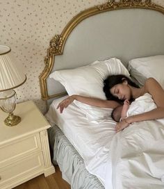 a woman laying on top of a bed under a white blanket next to a night stand