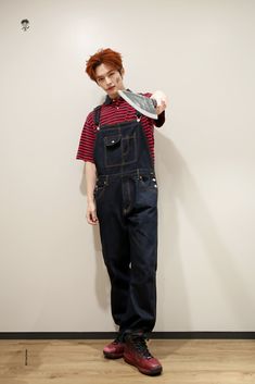 a man with red hair wearing overalls standing in front of a wall