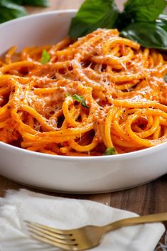 a white bowl filled with pasta and sauce on top of a wooden table next to silverware