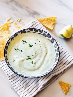 a bowl filled with white sauce surrounded by tortilla chips and lime wedges