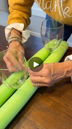 someone is making candles out of green paper on a wooden table with wine glasses and napkins