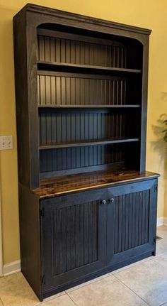 a black bookcase sitting in the corner of a room next to a potted plant