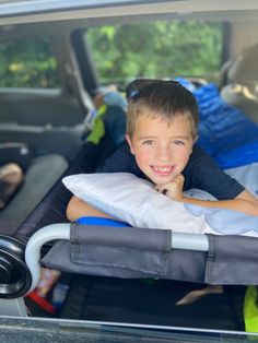 a young boy laying in the back of a car seat with his pillow on it