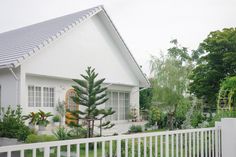 a house with a white picket fence and trees in the front yard on a cloudy day