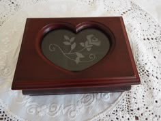 a small wooden box with a heart on it's lid sitting on a doily