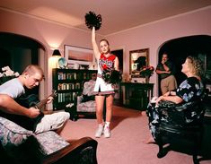 a girl in a cheerleader outfit is playing the guitar while two other people watch