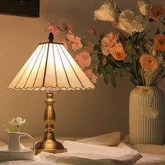 a table lamp sitting on top of a bed next to a vase filled with flowers