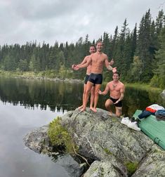 two shirtless men standing on top of a rock next to a body of water