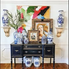 blue and white vases sit on top of a table in front of a painting