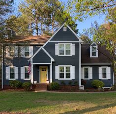 a blue house with white shutters on the front and yellow door is surrounded by trees