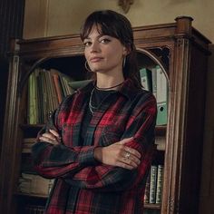 a woman standing in front of a bookcase with her arms crossed and looking off to the side