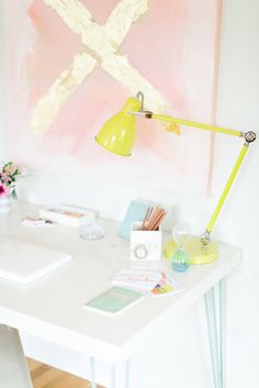 a white desk with a yellow lamp next to it and a painting on the wall