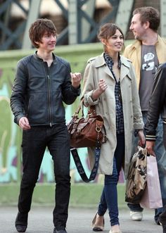 three people walking down the street talking to each other and one person holding a handbag