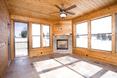 an empty living room with wood paneled walls and floor to ceiling windows that look out onto the snow covered field