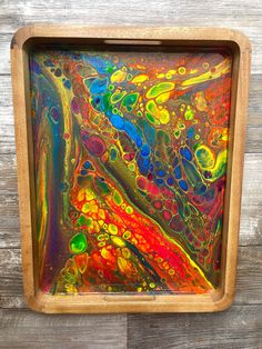 an abstract painting in a wooden frame on a wood wall with paint pouring over it