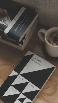 two books sitting on top of a wooden table next to a cup of coffee