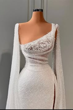 a white wedding dress with long sleeves and an open back, on display in front of a mannequin