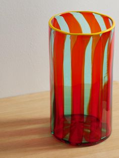 a red and green striped glass sitting on top of a wooden table next to a white wall