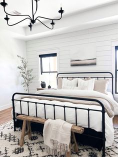 a bedroom with white walls and black metal bed frame, pillows, blankets, and rugs