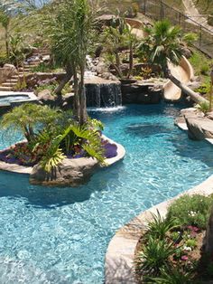 an outdoor swimming pool surrounded by palm trees and other tropical plants, with slides in the background