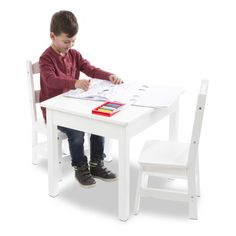 a young boy sitting at a white table and chair with papers on the table next to him