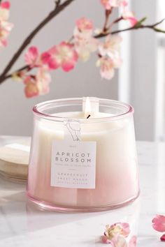 a white candle sitting on top of a table next to pink flowers and a plate