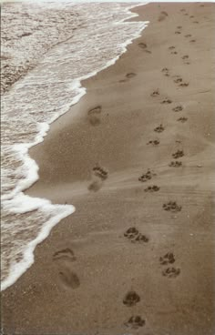 two footprints in the sand next to an ocean beach with waves coming in and one person walking along