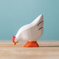 a small wooden toy bird with an orange beak sitting on a table next to a blue wall