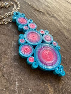 a necklace with pink and blue circles hanging from it's side on a wooden surface