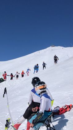 skiers and snowboarders on the side of a snowy hill with blue sky