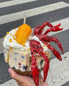 a person holding up a cupcake with lobsters on top and whipped cream in the middle