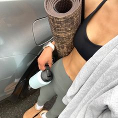 a woman is holding a yoga mat near a car