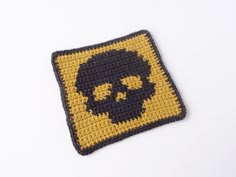 a crocheted square with a black and yellow skull in the center on a white surface