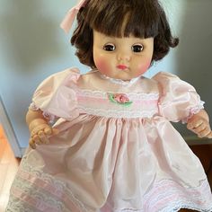 a doll with brown hair wearing a pink dress and holding her hands out to the side