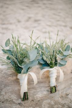 two white vases filled with flowers and greenery on top of a stone floor