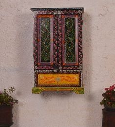 an artisticly painted window on the side of a white building with potted plants