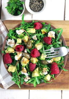 a salad with raspberries, avocado and feta cheese on it