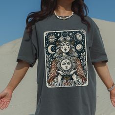 Step into a world of mysticism and cosmic beauty with our 'The Sun' tarot card t-shirt, designed on the soft and durable Comfort Colors tee. This vintage-style graphic features the powerful symbol of the Sun, a tarot card that represents positivity, vitality, and joy. Perfect for astrology enthusiasts, spiritual seekers, and boho fashion lovers, this shirt combines earthy tones with an intricate celestial design. The high-quality print and comfortable fit make it a stylish yet thoughtful gift for anyone drawn to the mysteries of the cosmos. High-Quality Comfort Colors Shirt: Known for its soft, broken-in feel and classic fit. Unique Design: Perfect for yoga lovers, meditators, or anyone on a spiritual journey. Unisex Fit: Ideal for both men and women with a relaxed, comfortable fit. Durabl Tarot Card Tshirts, Tarot T Shirt, Celestial Clothing, Sun Tarot Card, Tarot Card Shirt, The Sun Tarot Card, The Sun Tarot, Vintage Tarot, Celestial Design