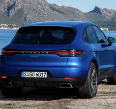 the rear end of a blue porsche cayenne parked in front of a body of water