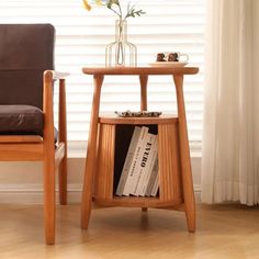 a wooden table sitting next to a chair with a book on it and a vase filled with flowers