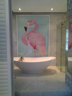 a bathroom with a bathtub and pink flamingos on the wall behind glass doors