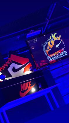 the nike logo is lit up at night in front of two televisions with logos on them