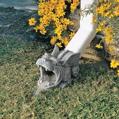 a statue of a dragon on the ground next to yellow flowers and a white pole