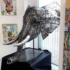 an elephant sculpture sitting on top of a black table next to pictures and paintings hanging on the wall