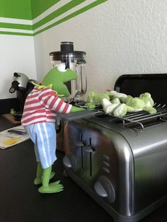 the kermik frog is standing next to an open toaster oven with vegetables on it