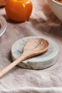 a wooden spoon sitting on top of a marble plate next to a bowl of fruit