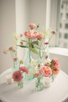 an image of flowers in glass vases on a white table with candles and windows